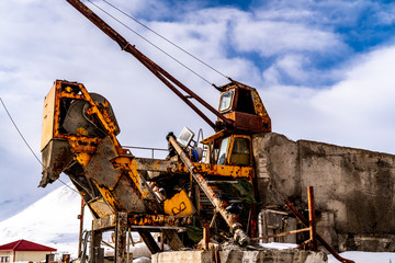 An old and rusty decommissioned crane attached to a concrete structure outdoors in from of a snowy landscape.