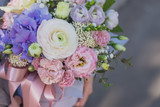 Fototapeta Storczyk - Flower arrangement in a pink hat box was created by a florist for a wedding gift. Flower bouquet of blue hydrangea, white Freesia, pink Ranunculus asiaticus, eustoma flowers, roses and eucalyptus