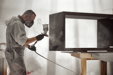 Wall Mural - Man Painting Furniture Details.  Painter with safety mask painting a wooden furniture with spray gun.