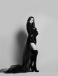 © Dmitry Lobanov - Young beautiful brunette woman in black clothes with long transparent hem and high boots standing and looking at camera