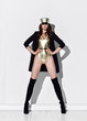 © Dmitry Lobanov - Young beautiful brunette woman in golden swimsuit, cap, black high boots and jacket standing over white wall