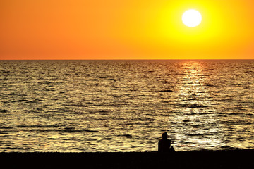Wall Mural - sea beach sunset sky landscape with female person enjoying hot summer evening on ocean shore against