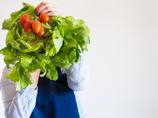 Delivery girl or small shop owner wearing blue apron holding fresh produce - fresh vegetables, pasta and milk - in gloved hands. Food delivery, local grocery shopping