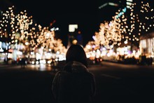 Rear View Of Woman Standing On City Street Against Christmas Lights At Night