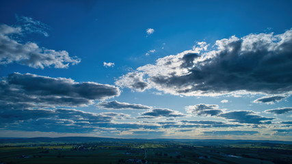 Wall Mural - Blue sky and multiple clouds background showing a horizon and a hidden sun