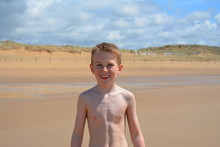 Portrait Of Happy Shirtless Boy Standing At Beach Against Sky On Sunny Day