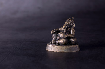 Ganesh, hindu god of success. Little statue of bronze Ganesha against dark grey background.