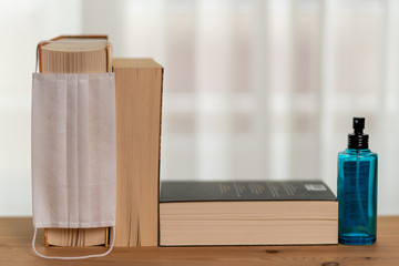 There are three books on the shelf in front of the window curtain, one spray cologne, one surgical mask on the shelf. 