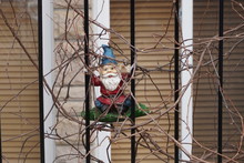 A Gnome That Is Making A Smile. Around A Black Fence And A Building Behind.