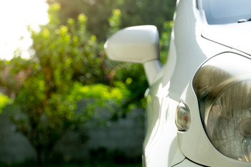 Beside front view of white car parking in the house with blurred nature green background.