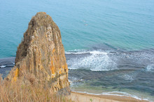 A High Cliff Hanging Over The Waves Of The Blue Sea. Several Gulls Are Circling Next To A Stone Cliff.