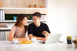 © iploydoy - Asian couple working together with laptop in morning and looking at each other. Breakfast and coffee on table.
