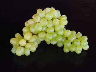 Sprigs of fresh green grapes on a black background closeup, copy space. Bright natural fruit template for printing and cover design