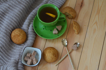 Wall Mural - A Cup of lemon tea, a warm sweater, cookies, and heart shaped brown cane sugar on a wooden table. A pleasant tea party in a cozy atmosphere at home