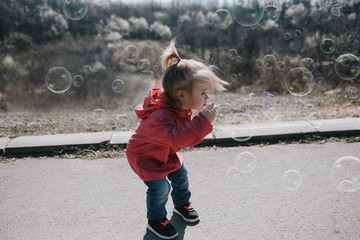 Two years old caucasian child girl blowing soap bubbles outdoor during a day - happy carefree childhood