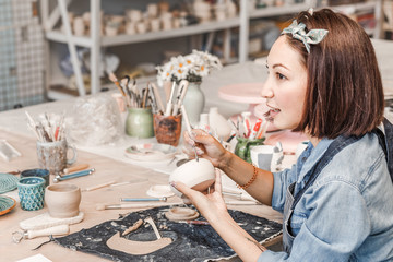 Wall Mural - girl craftsman working with earthenware product for sale in her shop. Pottery business concept for an artist concept