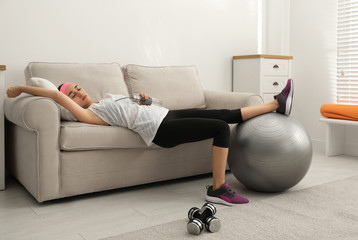 Canvas Print - Lazy young woman with sport equipment on sofa at home