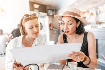 two girl friends carefully read menu, sitting in a cafe. small business and dining room concept