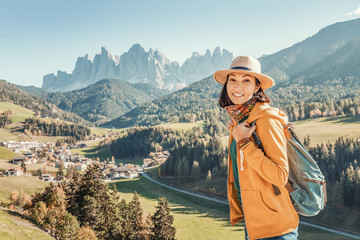 Wall Mural - Asian girl hiker walks along a special recreational trail high in the Alpine mountains. A cozy little village and rocky cliffs in the background