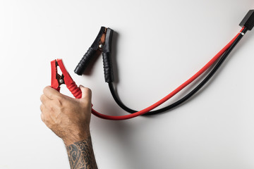 Man hand with tattoo holding red jumper cable isolated on white background