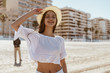 joyfully smiling girl holds hand hat on the background of beach sand and buildings