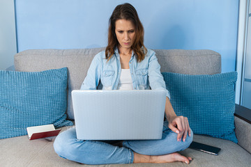 Woman sitting at the sofa indoors in home office with laptop computer.