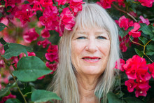 Happy Healthy Beautiful Senior Woman At Her 70-80 Beauty Portrait In Tropical Summer Smiling From The Flower Bush