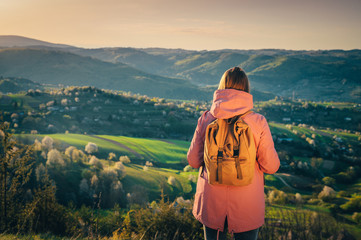 Adventure photo, journey hipster traveler. Female tourist or hiker looking at beautiful spring landscape in background. Traveling photo, vintage rucksack, backpack. Edit space for your quote 