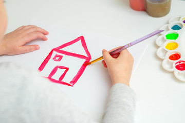 Wall Mural - Child is drawing red house with watercolors on the white sheet of paper.