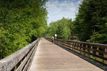 Wall Mural - Woman running down a long elevated boardwalk, blank sign for text, horizontal aspect