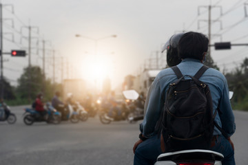 Rear side of motorbike with two people sitting. Parked in a traffic signal. Blurry picture of traffic passing through the front. Evening after work.