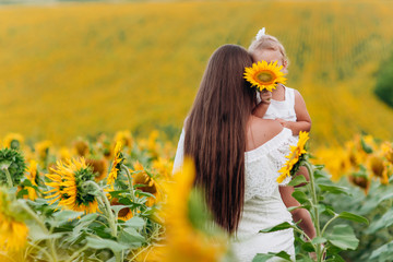 Wall Mural - Happy mother with the daughter in the field with sunflowers. mom and baby girl having fun outdoors. family concept.