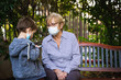 © progat - Grandmother and little kid playing with a smartphone in the backyard while wearing protective masks due to coronavirus outbreak