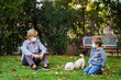 © progat - Grandmother and little kid playing with a smartphone in the backyard while wearing protective masks due to coronavirus outbreak