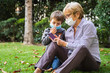 © progat - Grandmother and little kid playing with a smartphone in the backyard while wearing protective masks due to coronavirus outbreak