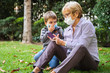 © progat - Grandmother and little kid playing with a smartphone in the backyard while wearing protective masks due to coronavirus outbreak