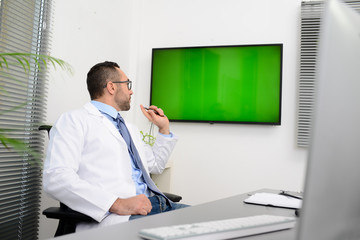 man male doctor professor teacher in medical office at desk with computer wearing white lab coat showing to students wall green srceen research covid19 and coronavirus seminar