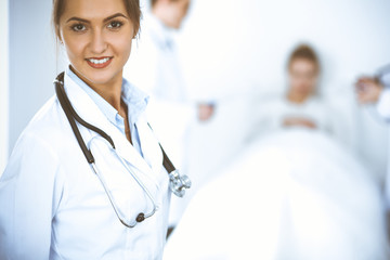 Wall Mural - Female doctor smiling on the background with patient in the bed and two doctors