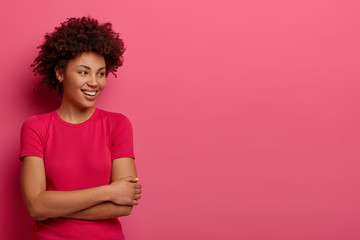 Wall Mural - Isolated shot of happy millennial girl looks gladfully away, dressed in casual wear, notices something funny right, stands against pink background, blank space for your advertising content or text