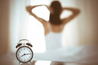 © rogerphoto - Woman stretching hands in bed after wake up, sun flare . Brunette entering a day happy and relaxed after good night sleep and back view. Concept of a new day and joyful weekend