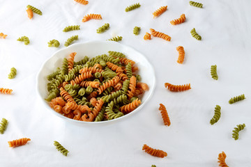 A white bowl with vegetable pasta orange and green color on a white linen tablecloth  