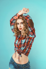 Pin-up girl with curly blond hair with red checkered bow and shirt wearing jeans shorts.