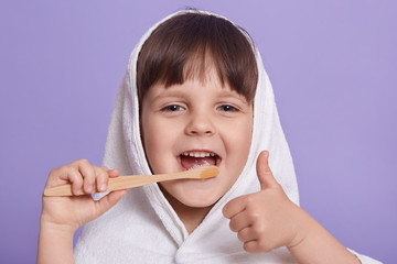 Wall Mural - Close up portrait of funny pleasant happy little girl making gesture, showing sign super, thumb up, having towel on head, brushing teeth, looking directly at camera. Childhood and emotions concept.