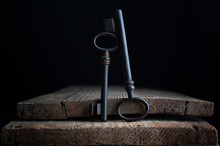  Two Old Keys Stand On Old Wooden Board On A Dark Background