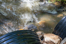 Overhead View Of Water Flowing Rapidly Out Of Two Large Black Drain Pipes, Environmental Pollution And Runoff, Horizontal Aspect