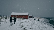 Two Men Walk In The Snow Along Path By The Sea