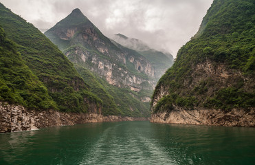 Wuchan, China - May 7, 2010: Dawu or Misty Gorge on Daning River. View into canyon between tall green covered mountains with some cliff sides around emerald green water under cloudscape.