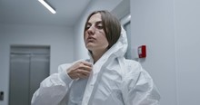 Tired Nurse Putting On Hazmat PPE Suit During Pandemic