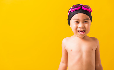 Summer vacation concept, Closeup portrait Asian happy cute little child boy wearing goggles and swimsuit, Kid having fun with in summer vacation looking camera, studio shot isolated yellow background