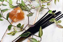 A Close Up Image Of Honey Calcite With Several Incense Sticks And Green Plant On A White Wooden Background. 